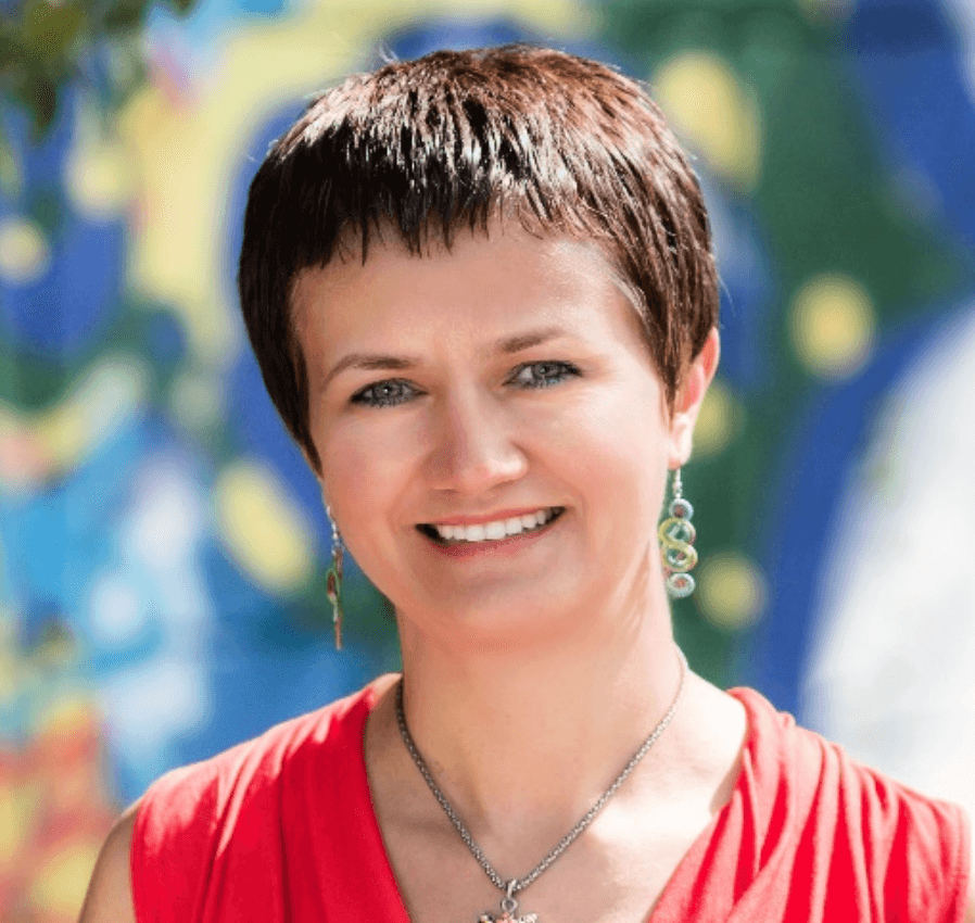 Smiling woman with short brown hair, wearing a red top and colorful dangling earrings.
